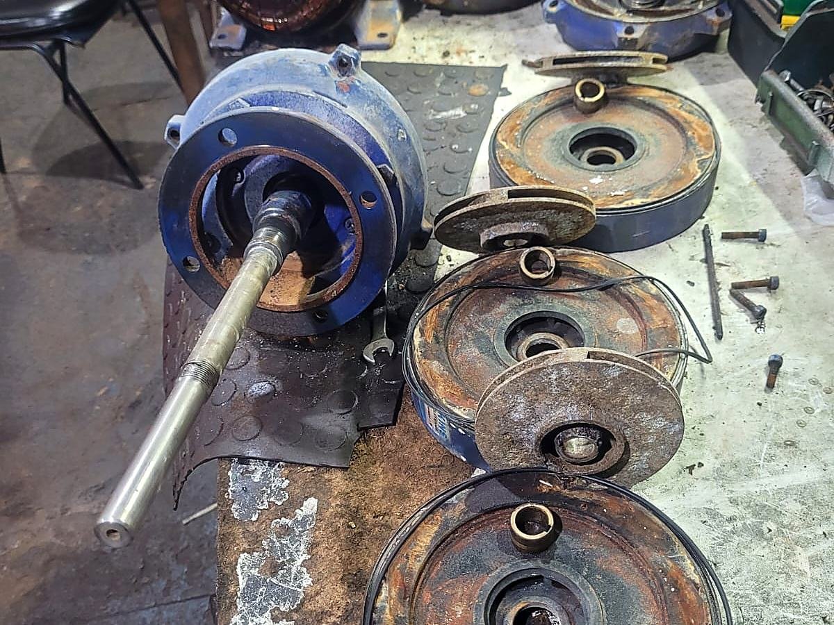 Bomba d'água desmontada na bancada, com eixo, rolamento, tampa e rotores separados para diagnóstico